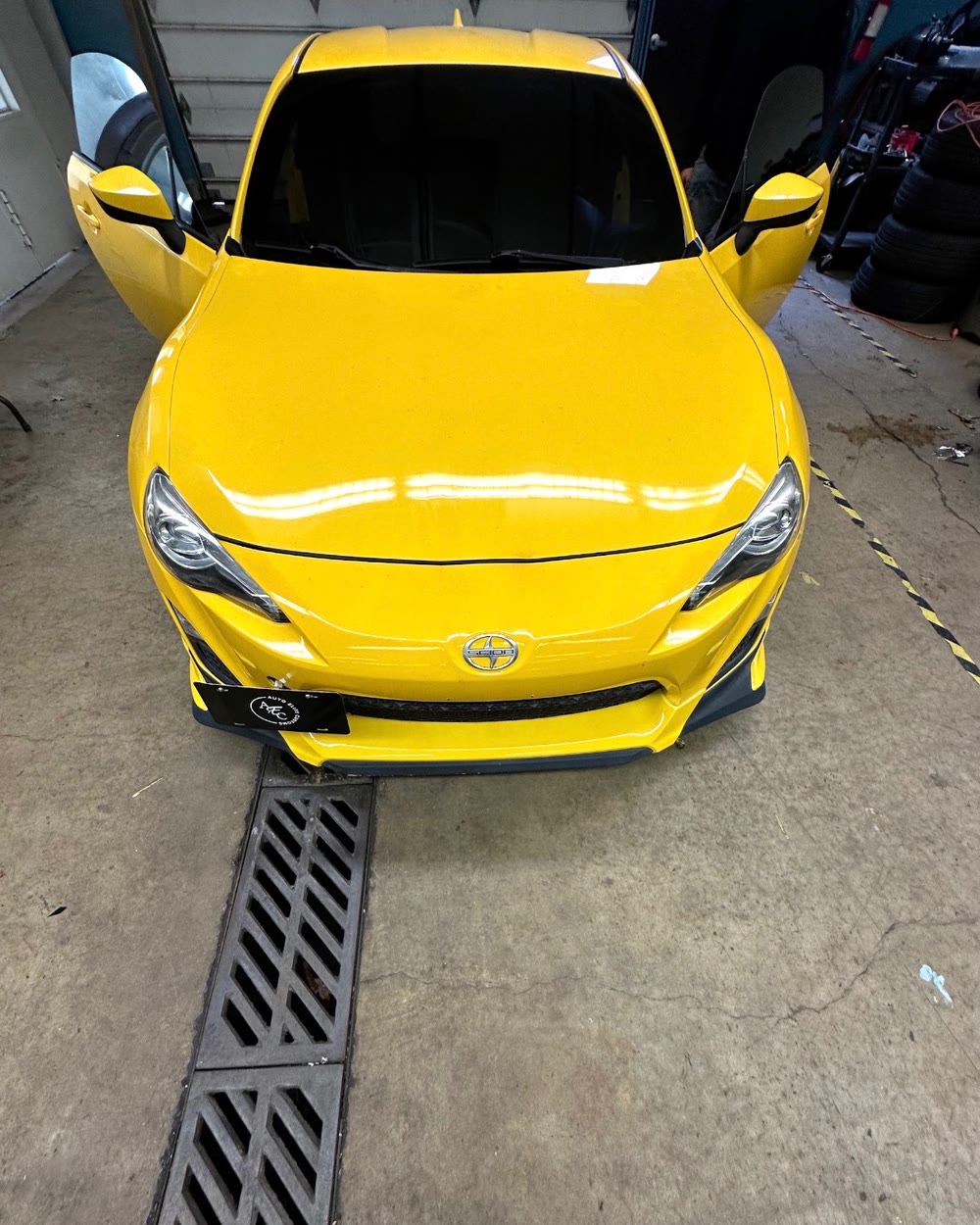 Yellow Scion in the work bay with finished dark windshield and side glass