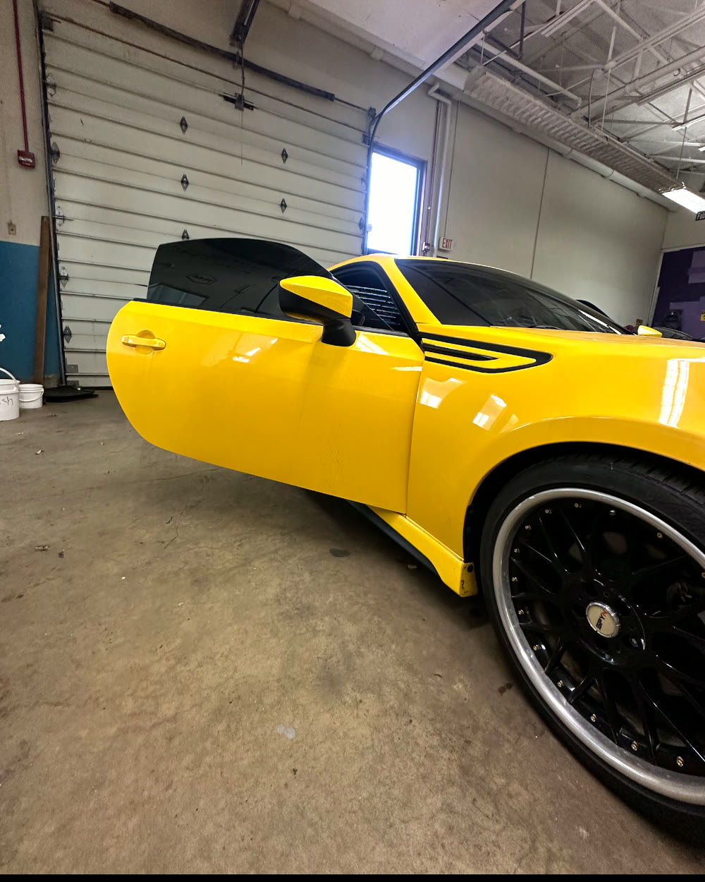 Yellow Scion inside the bay with the driver door open and dark side glass visible